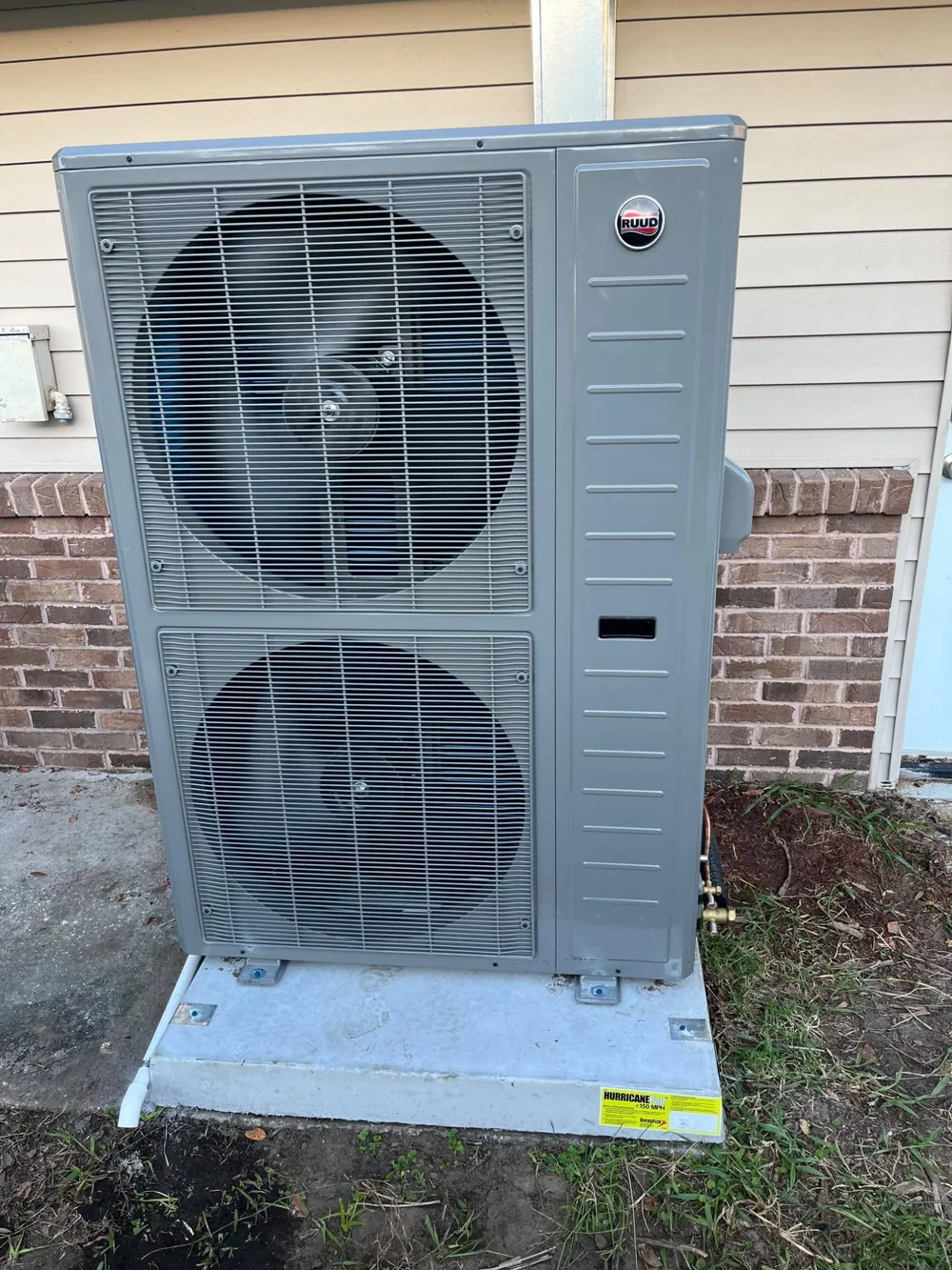 New Ruud dual-fan outdoor HVAC unit on a hurricane-rated pad beside a Wesley Chapel home